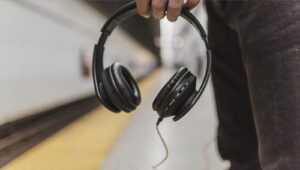 A person standing at a train station, holding headphones.