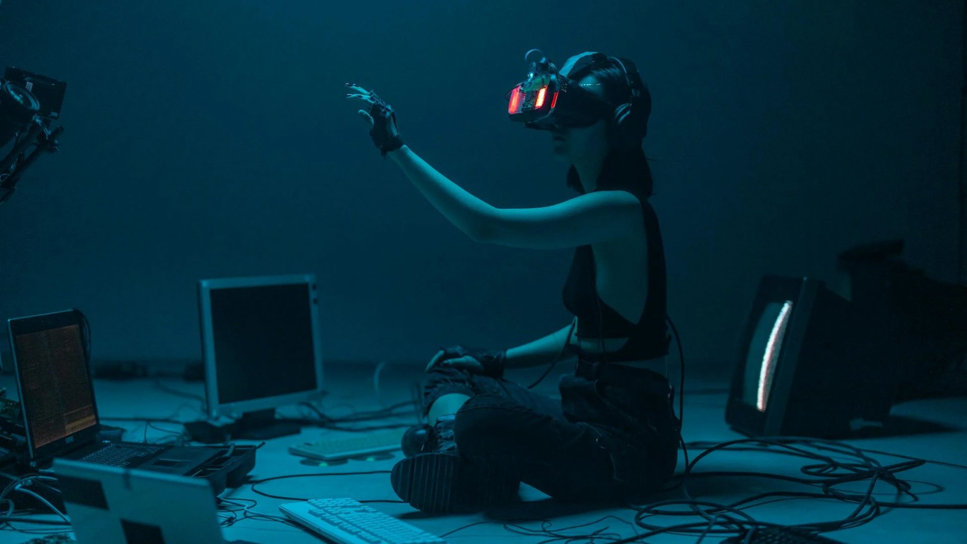 A girl, sitting down in the middle of a bunch of computers while wearing VR headsets as a representation of AI In Daily Life and Marketing