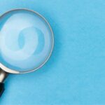 A magnifying glass over a light blue surface as a symbol of how careful we should be when analyzing the content we see online, how media literacy is important and how AI-generated content does require us to acquire new skills.