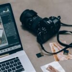 A Laptop, a Camera and some pictures on the floor, representing the content creation process.