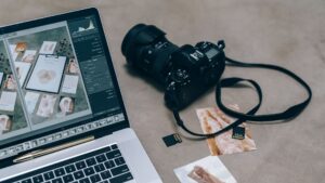 A Laptop, a Camera and some pictures on the floor, representing the content creation process.