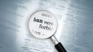 A magnifying glass on top of a dictionary page. It is highlighting the word "Ban"