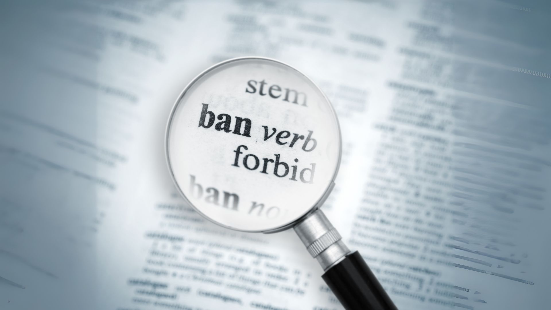 A magnifying glass on top of a dictionary page. It is highlighting the word "Ban"