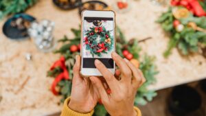 A picture of someone taking a picture of a holiday wreath on a table along with other holiday decorations. Probably to use it as holiday content for socials.
