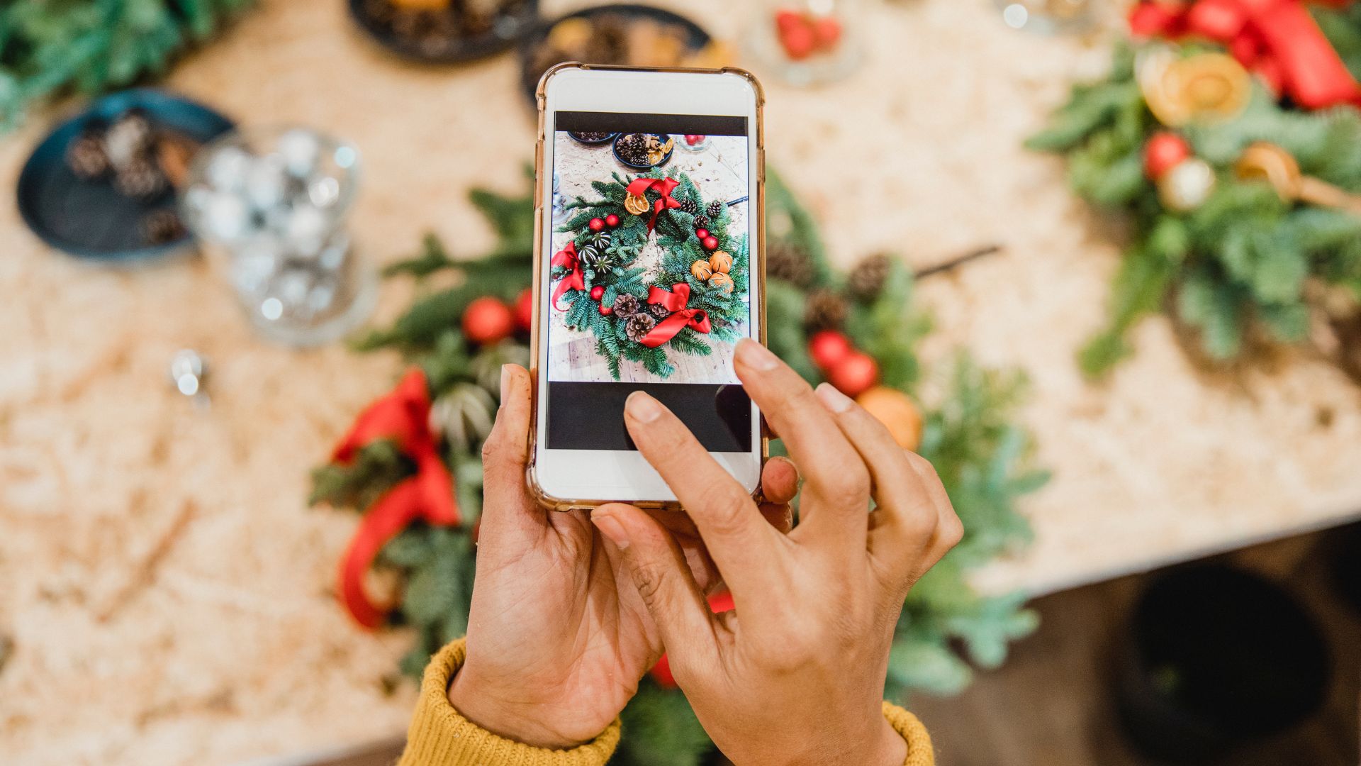 A picture of someone taking a picture of a holiday wreath on a table along with other holiday decorations. Probably to use it as holiday content for socials.