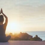 A curly haired girl doing a yoga pose while looking at the sunset representing the focus we will need for 2026